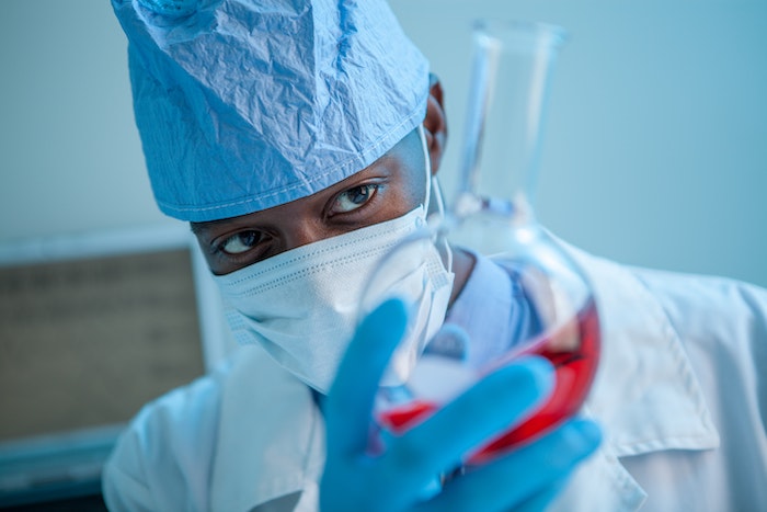 scientifique qui manie une fiole avec un liquide rouge a l'interieur